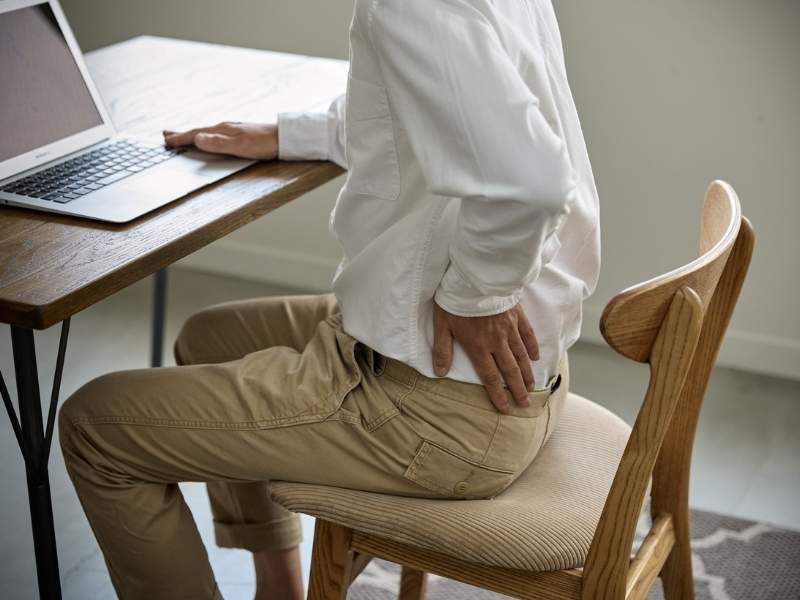A Melhor Cadeira para Coluna Lombar: Guia Científico para Proteção da Saúde Postural 2 Uma pessoa sentada em uma cadeira para coluna inadequada.